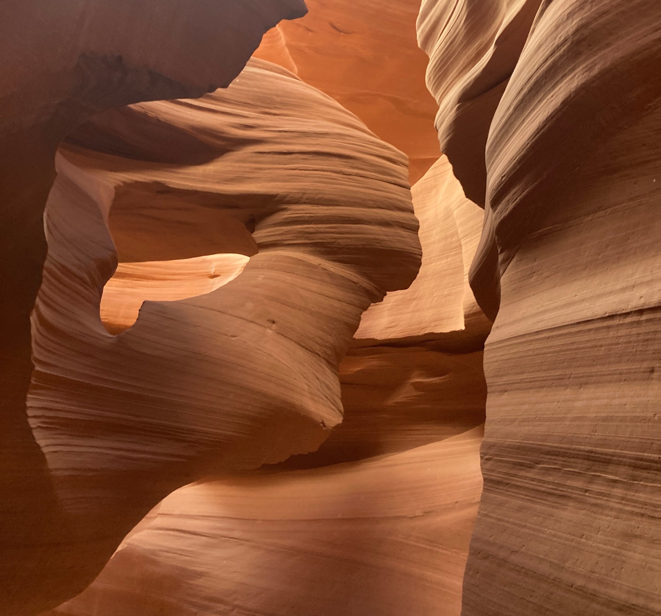 A detailed close-up of swirling, deep-orange sandstone in a slot canyon, focusing on a narrow, bright white opening of light at the to